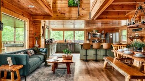 Interno di una baita in legno con zona giorno, cucina e sala da pranzo, caratterizzato da ampie finestre e pavimenti in legno.