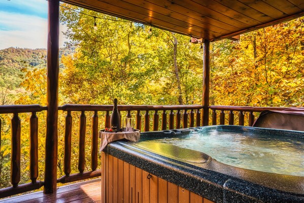 A hot tub on a wooden deck with a view of autumn trees.