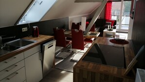 Een compacte keuken met een eethoek, een inbouwvaatwasser en een raam met een rood gordijn.
