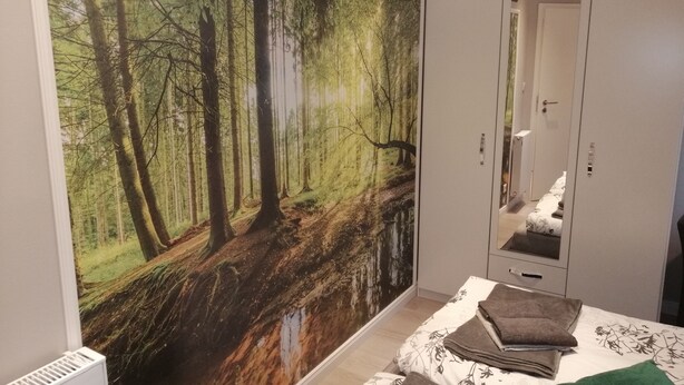 Een slaapkamer met een grote bosmuur, een bed met een bloemenbedekking en een kledingkast.