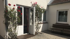 A patio area with a bench, a door, and potted plants with red flowers.