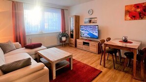 A cozy living room with a sofa, coffee table, TV, and dining area.