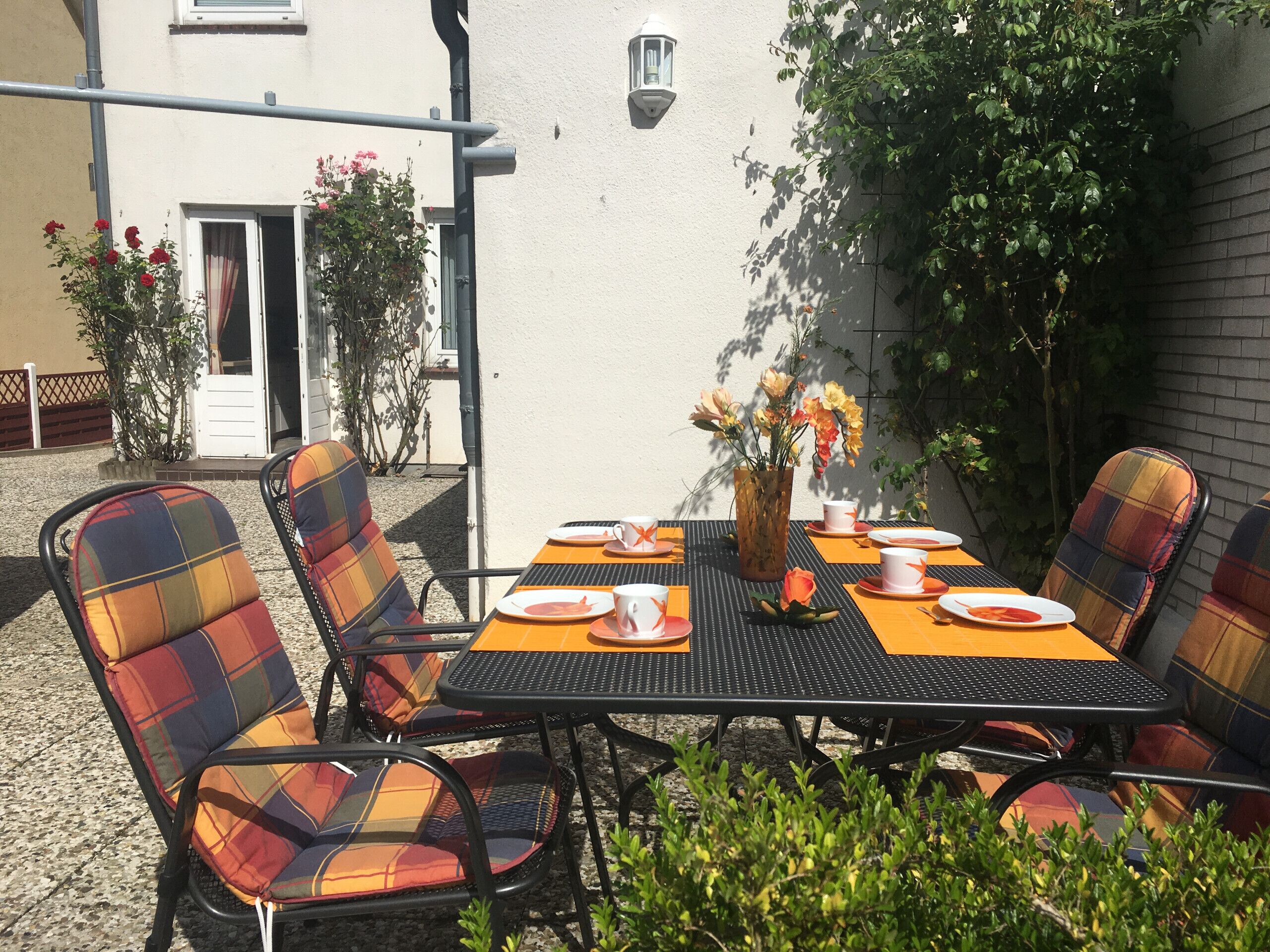 Eine Terrasse im Freien mit einem für vier Personen gedeckten Tisch, umgeben von karierten Stühlen.