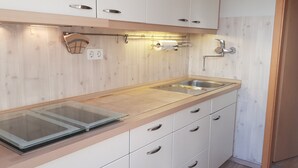 A modern kitchen with a glass cooktop, stainless steel sink, and wooden cabinetry.