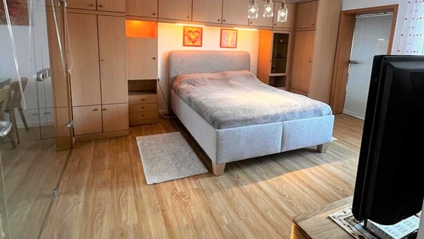 A bedroom with a bed, wooden wardrobe, and a television on a wooden stand.