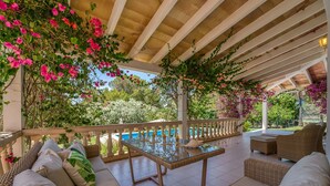 A covered outdoor seating area with wicker furniture, a glass table, and a pool in the background. - Finca near the beach Casa Bonita in Mallorca (Colònia de Sant Jordi)