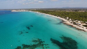 An aerial view of a coastal area with clear turquoise waters, a sandy beach, and a small settlement with buildings. - Finca near the beach Casa Bonita in Mallorca (Colònia de Sant Jordi)