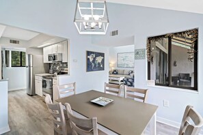 Una cucina moderna con mobili bianchi, un frigorifero in acciaio inossidabile e una zona pranzo con tavolo marrone e sedie di legno.
