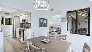 Una cucina moderna con elettrodomestici in acciaio inossidabile, un'area pranzo con tavolo marrone e sedie bianche, e un'ampia finestra con vista sull'esterno.