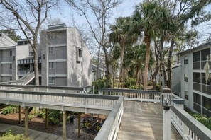 Un immeuble résidentiel doté d’une terrasse en bois, entouré de palmiers et d’autres plantes.