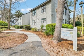 Un edificio residenziale a più piani con un cartello che indica 'UNITS 101-7710' e un vialetto lastricato che conduce all'ingresso.