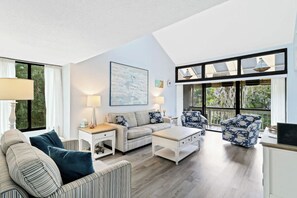 Ein geräumiges Wohnzimmer mit hohen Decken, großen Fenstern und Blick ins Freie.