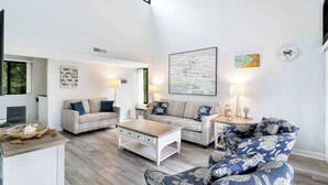 Un soggiorno spazioso con soffitto alto, una grande finestra e vista sull'esterno. Si notano due divani, un tavolino da caffè e un tavolino laterale con oggetti decorativi.