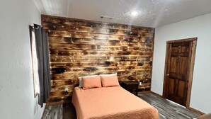 Une chambre à coucher avec un lit, un lambris en bois, une porte et une fenêtre avec des rideaux.