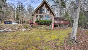 Une cabane avec des fondations en pierre, une terrasse en bois et une grande partie avant dotée de larges fenêtres.
