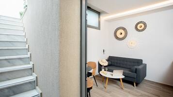Una sala de estar moderna con un sofá gris, una mesita redonda y una mesa de centro. Se observa una escalera que conduce a otro nivel.