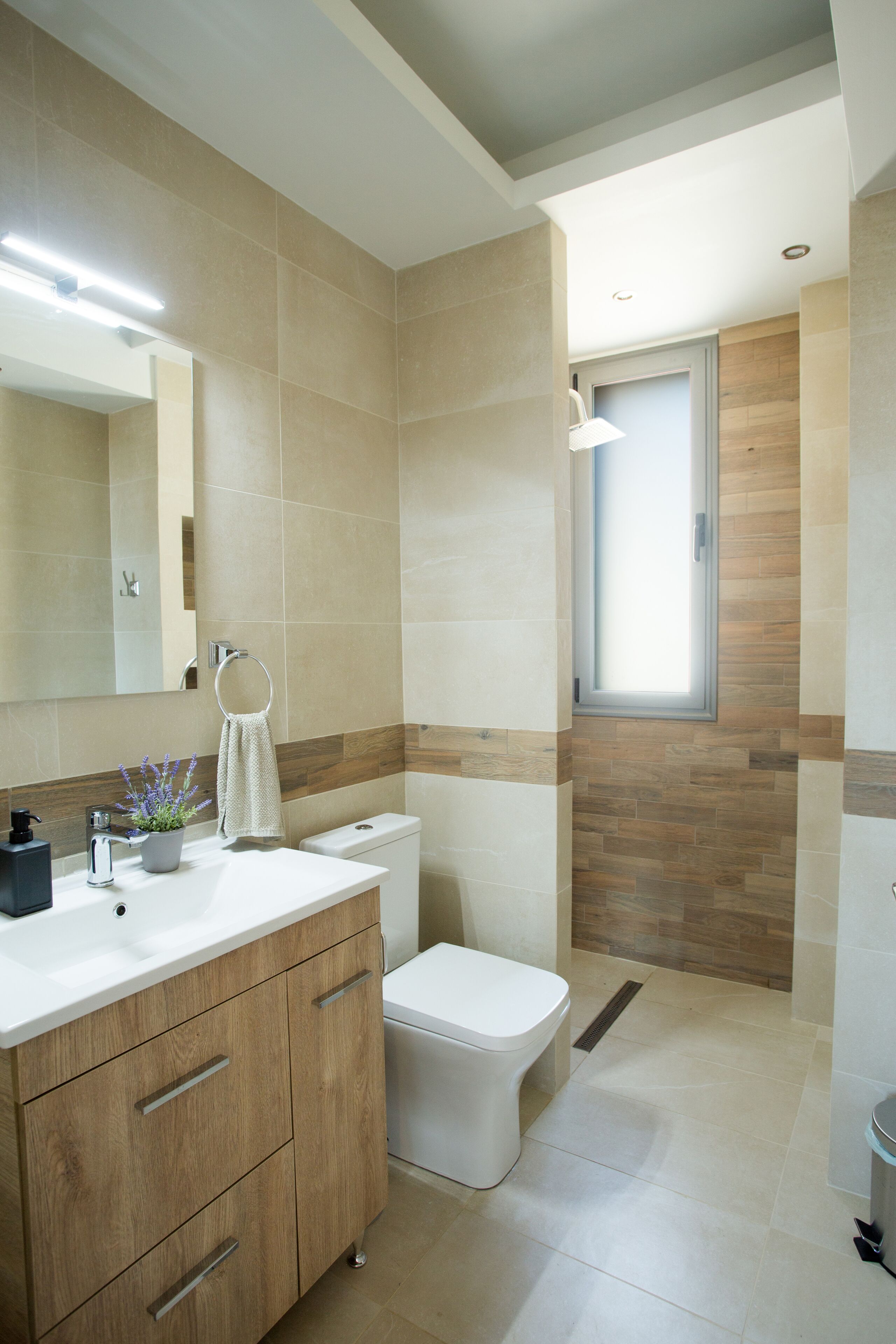 Un baño moderno con lavamanos blanco, tocador de madera y un inodoro.