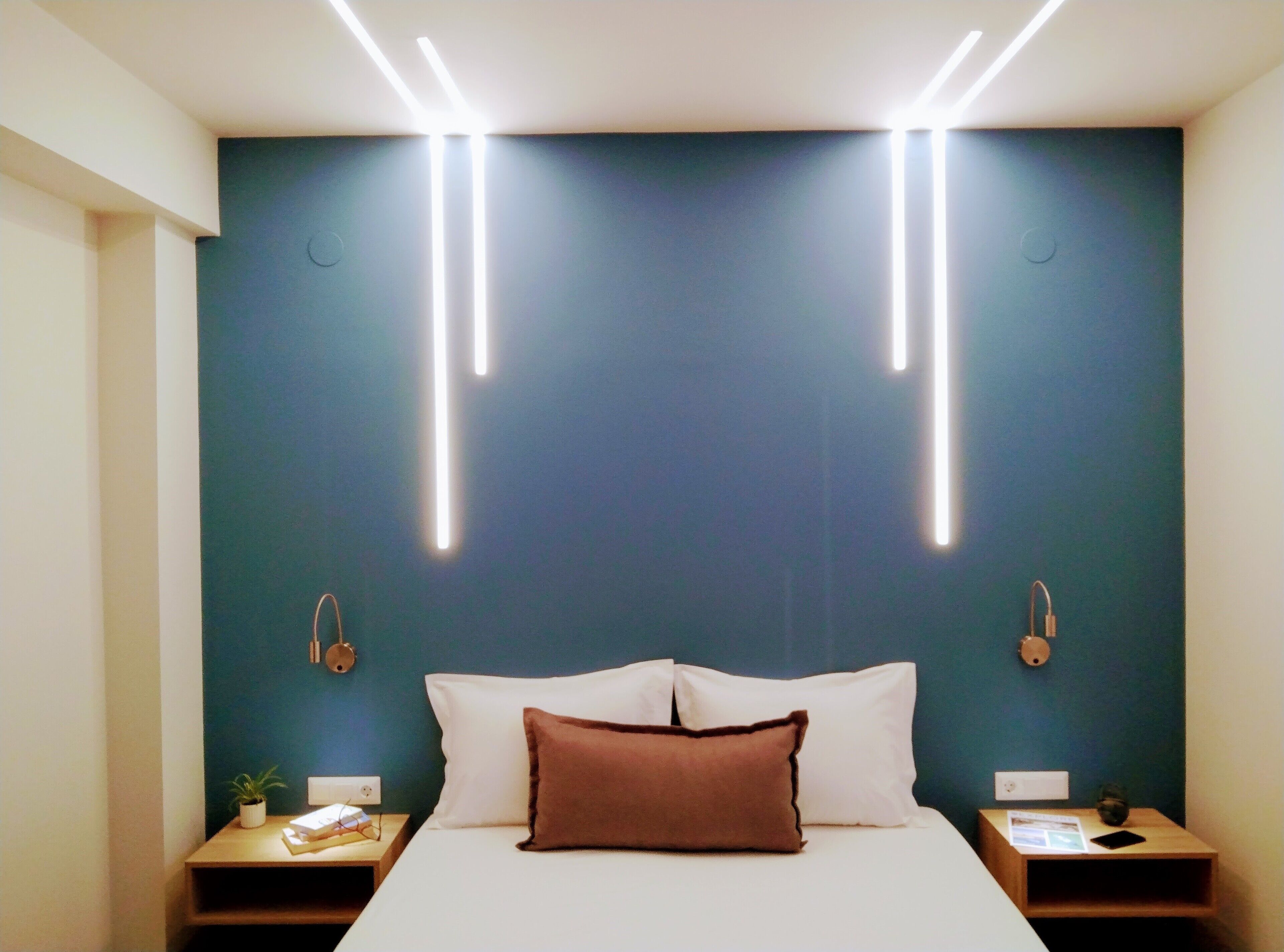 A modern hotel room with a large bed, bedside tables, and a wall-mounted light fixture.