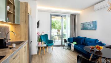 A modern living room with a blue sofa, a round coffee table, and a kitchen area with wooden cabinets and a built-in oven.
