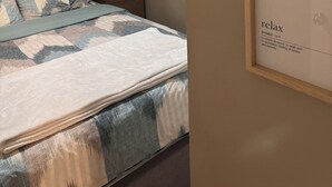Ett sovrum med en säng, en byrå, en målning som föreställer en stadsbild och inramad text på väggen.