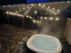 An outdoor hot tub area with a canopy and string lights, surrounded by a wooden fence.