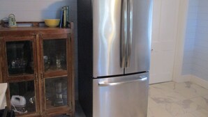 A stainless steel refrigerator in a kitchen with a wooden cabinet and a white door in the background. - Beautiful vintage cottage remodeled in Old Ocean Springs (Ocean Springs)