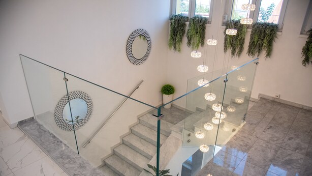 A modern staircase with glass railings, a decorative mirror, hanging plants, and pendant lighting. - La Luna ⭐⭐⭐⭐⭐ Rustic Deluxe Apartment with Pool & Jacuzzi Bikes and Parking (Našice)
