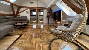 A spacious loft with high ceilings, wooden beams, a large sofa, a hanging chair, and a television. - La Luna ⭐⭐⭐⭐⭐ Rustic Deluxe Apartment with Pool & Jacuzzi Bikes and Parking (Našice)