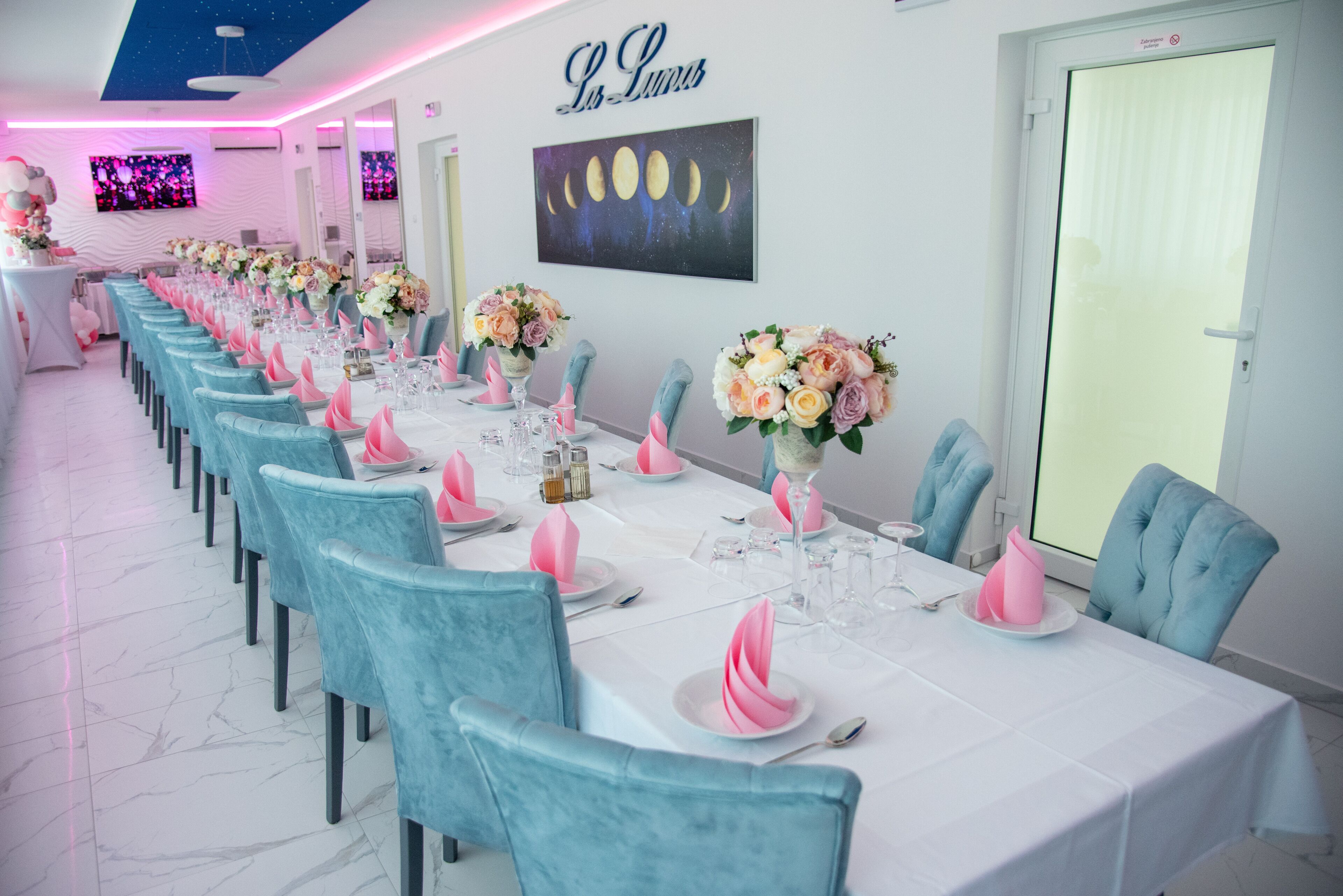 A long dining table with teal chairs, pink napkins, and floral centerpieces.