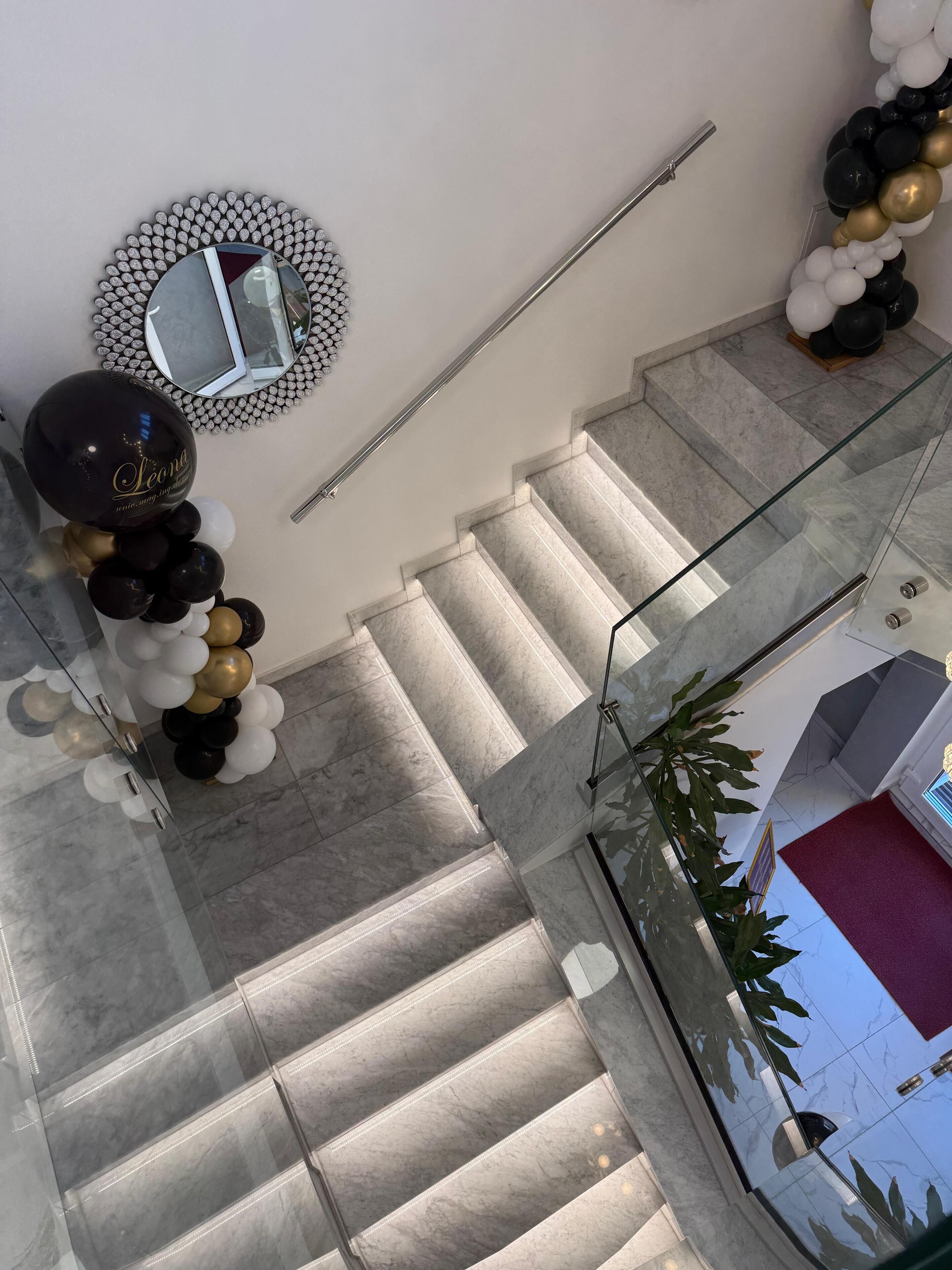 Una scala con gradini in marmo, ringhiera in vetro e un'elegante composizione floreale a forma di palloncino.