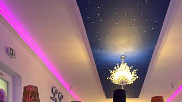Four bottles of wine on a glass table in a room with purple lighting and a chandelier.