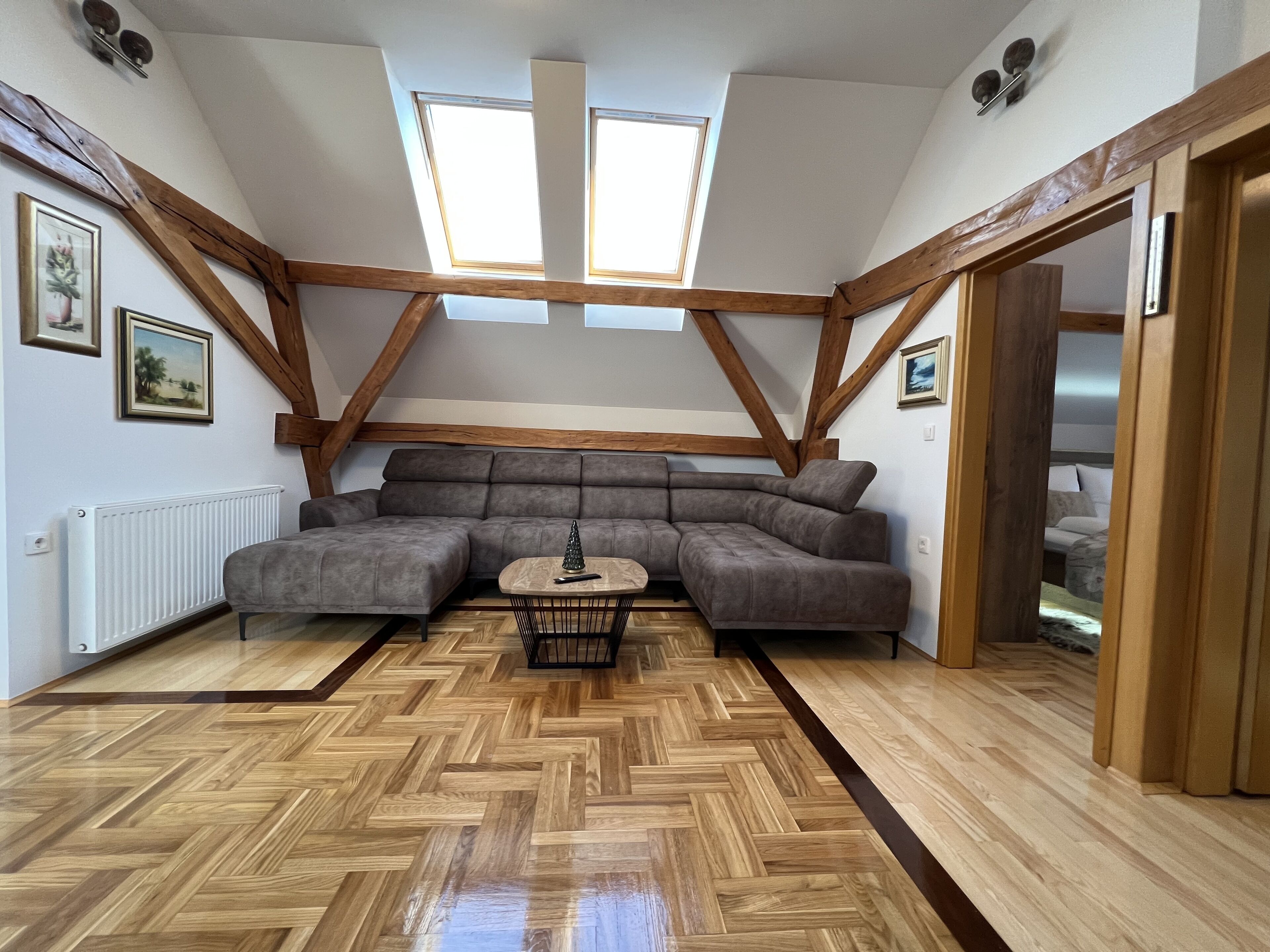 A loft-style room with a herringbone-patterned wooden floor, a gray sectional sofa, and a small round table with a decorative item.