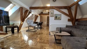 A spacious loft with a high ceiling, wooden beams, a large TV, a sofa, a dining table, and a chair. - La Luna ⭐⭐⭐⭐⭐ Rustic Deluxe Apartment with Pool & Jacuzzi Bikes and Parking (Našice)