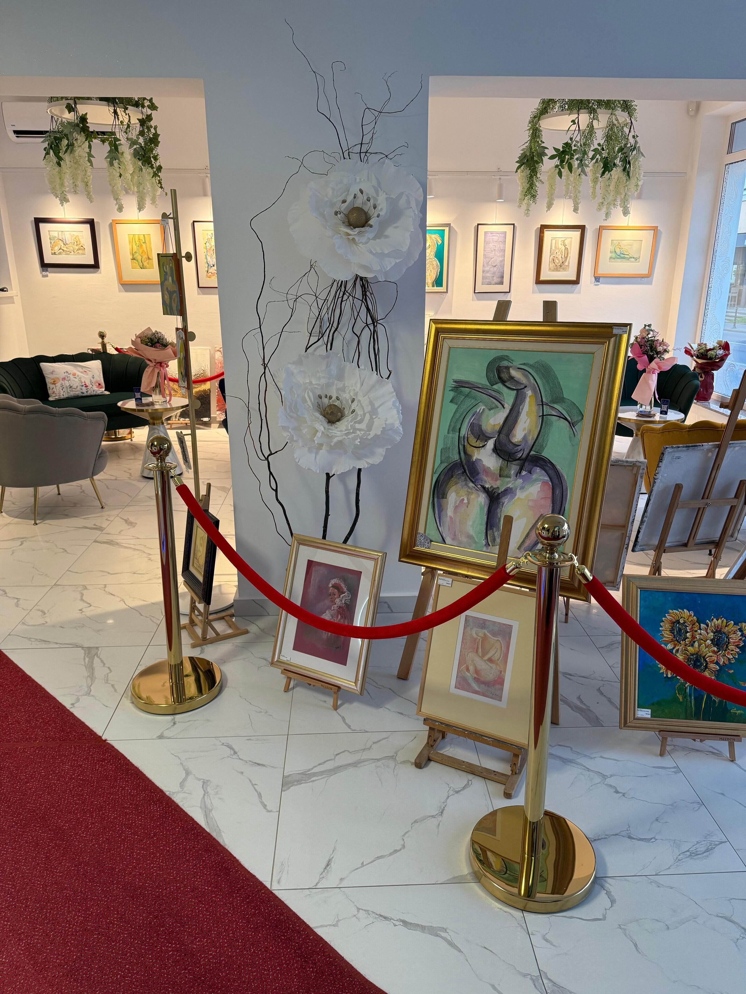 Una galería con obras de arte enmarcadas expuestas, una barrera de cuerda roja y un sofá verde al fondo.