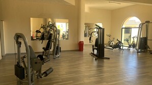 Ein großzügiger Fitnessraum mit verschiedenen Trainingsgeräten, Holzboden und großen Fenstern für natürliches Licht.