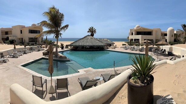 Ein Poolbereich mit Liegestühlen und Sonnenschirmen, umgeben von Palmen und Blick auf den Strand.