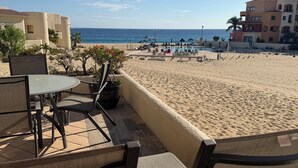 Eine Terrasse am Strand mit Tisch und Stühlen, mit Blick auf einen Sandstrand und den Ozean.