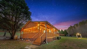 Uma cabana de madeira com varanda, rodeada por árvores e um céu estrelado.