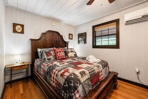 A bedroom with a wooden bed, a nightstand, a window with blinds, and a wall-mounted air conditioner.
