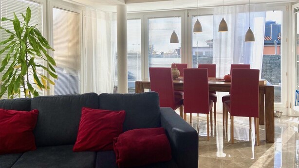 A modern living room with a dark sofa, red cushions, and a dining area with red chairs and a wooden table. - Ferienwohnung Riva - Wohlfühloase in Ruhiger Lage (Lindau)
