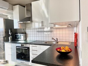 Une cuisine moderne avec des meubles blancs, un plan de travail noir, un évier en acier inoxydable et un saladier rempli de citrons.