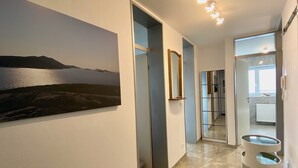 A modern hallway with a large landscape painting, a mirror, and a glass partition leading to a bathroom. - Ferienwohnung Riva - Wohlfühloase in Ruhiger Lage (Lindau)