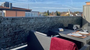 An outdoor dining area with stone walls, wicker furniture, and a table set for two. - Ferienwohnung Riva - Wohlfühloase in Ruhiger Lage (Lindau)