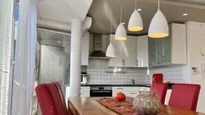 A modern kitchen with white cabinets, a wooden dining table, and red chairs. - Ferienwohnung Riva - Wohlfühloase in Ruhiger Lage (Lindau)