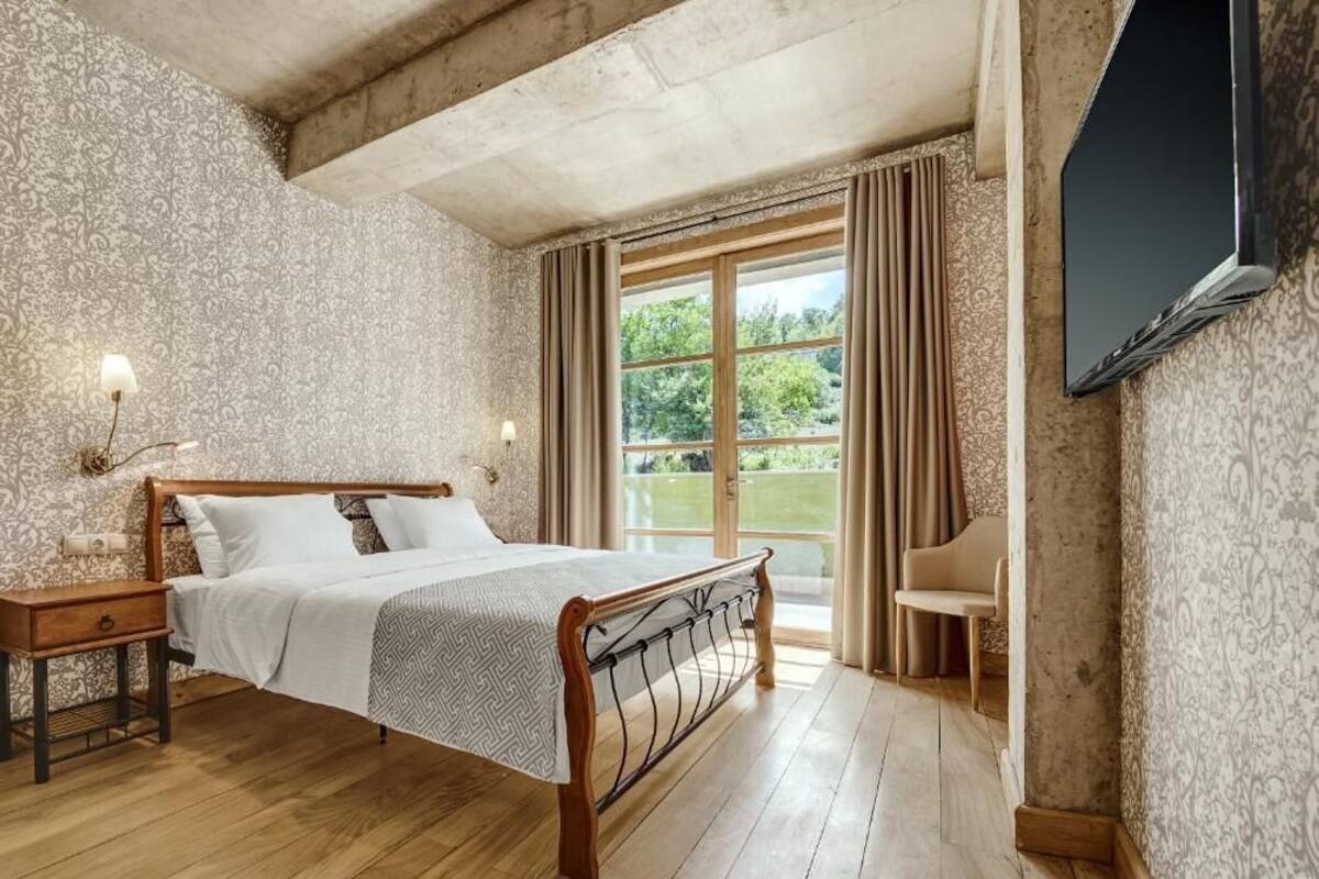 A bedroom with a wooden bed, a nightstand, a chair, and a TV mounted on the wall.