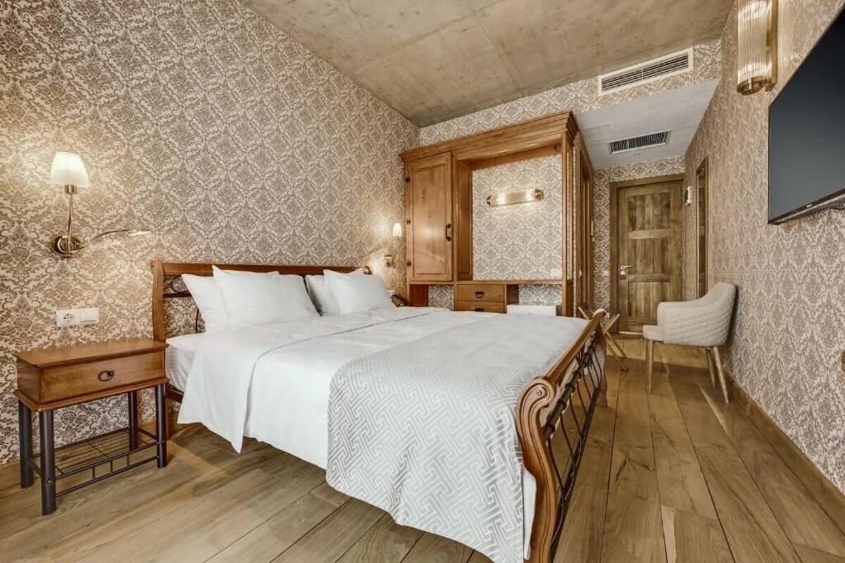 A bedroom with a wooden bed, a nightstand, a wardrobe, a chair, and a television.