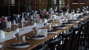 A long dining table set for a meal with chairs, a chandelier, and large windows. - Ampelo Resort (Gurjaani)