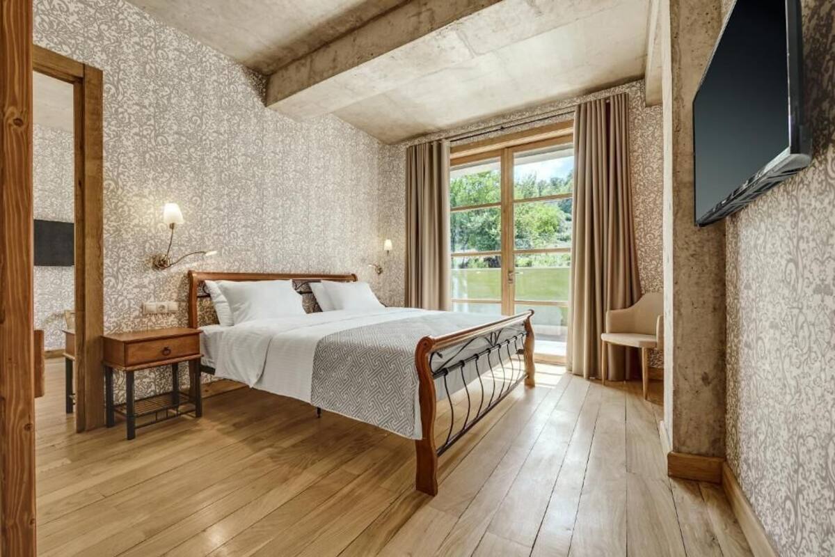 A bedroom with a wooden bed, a nightstand, a TV mounted on the wall, and a window with curtains.