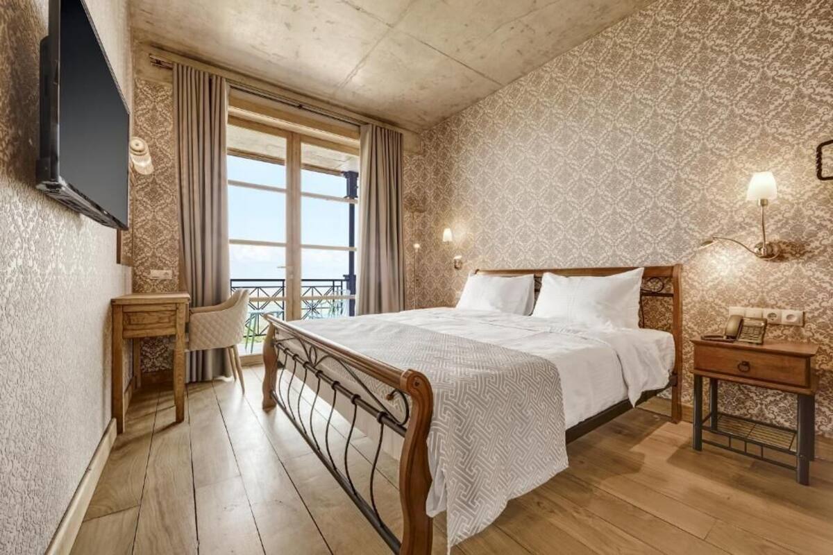 A bedroom with a wooden bed, a bedside table with a lamp, a TV mounted on the wall, and a window with curtains.