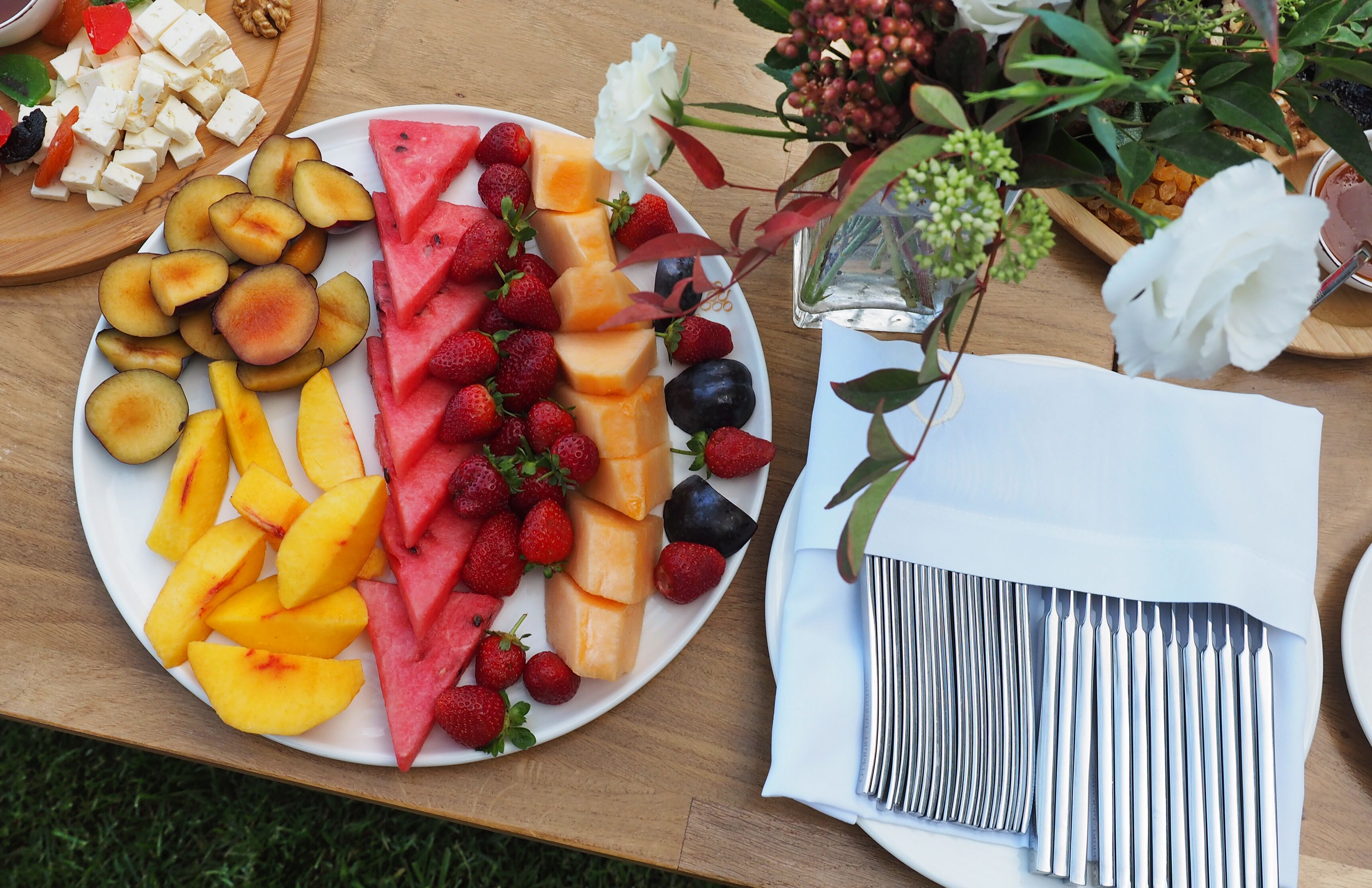 Una mesa con una bandeja de frutas, un vaso de agua y una servilleta con cubiertos.